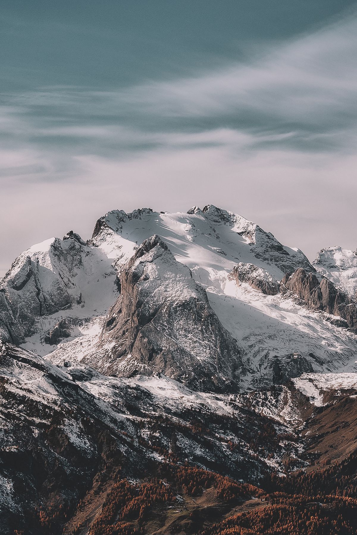 Schneebedeckter Alpengipfel über herbstlichen Wäldern