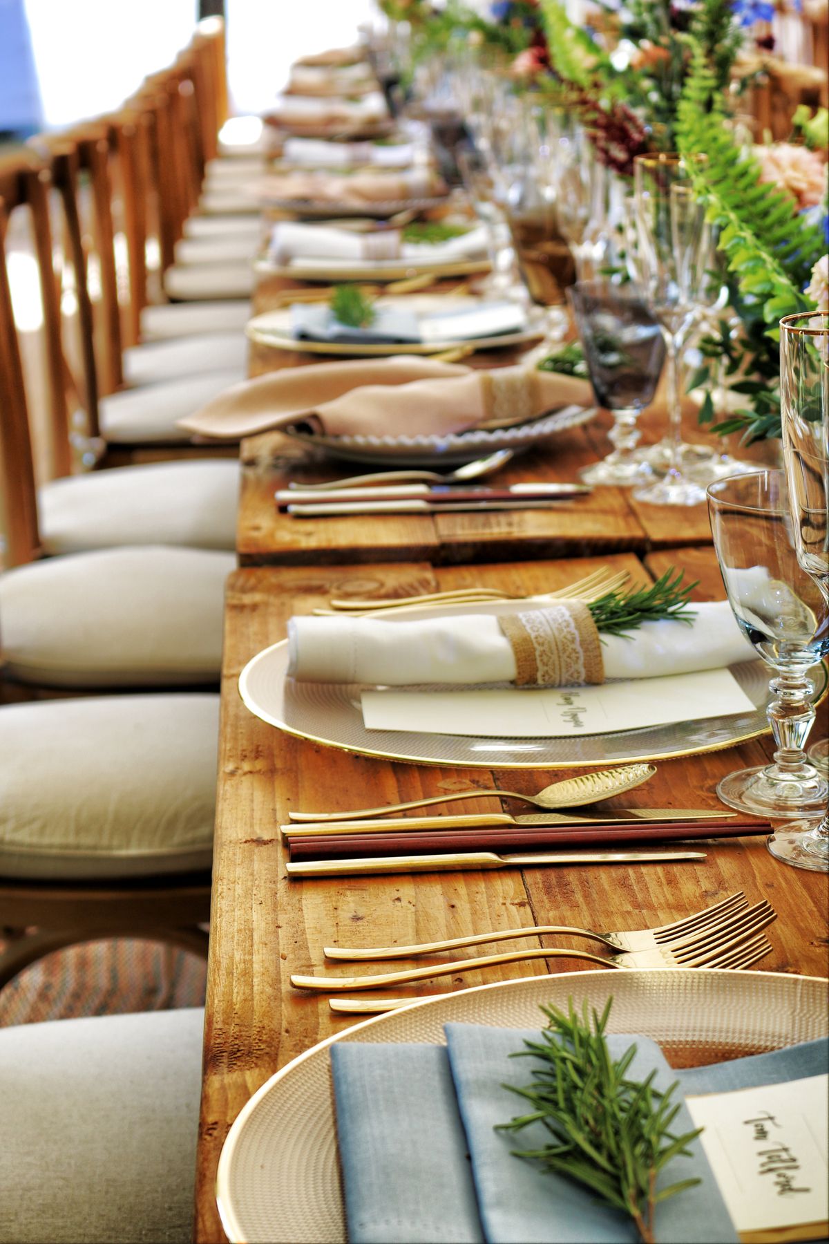 Lange Holztafel mit goldenem Besteck und Rosmarinzweigen